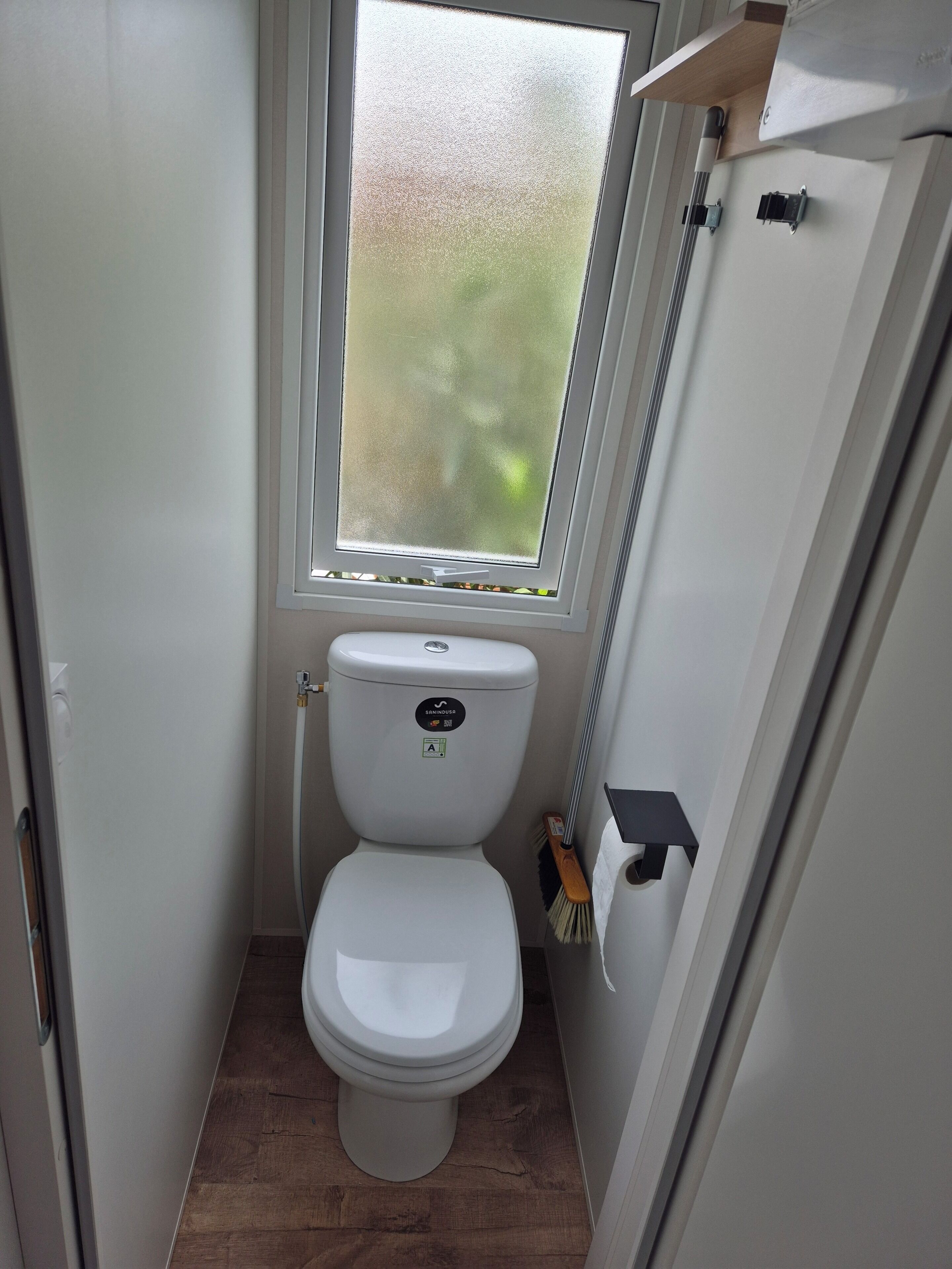 A compact bathroom with a toilet, a window, and a broom.