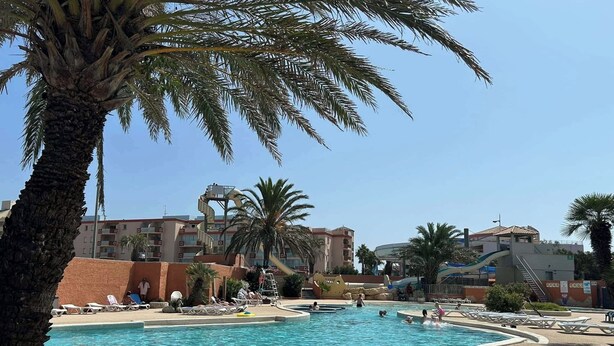 A pool area with palm trees, lounge chairs, and a water slide. - Mobile home near the sea, Camping 4* Mar Estang (Canet-en-Roussillon)