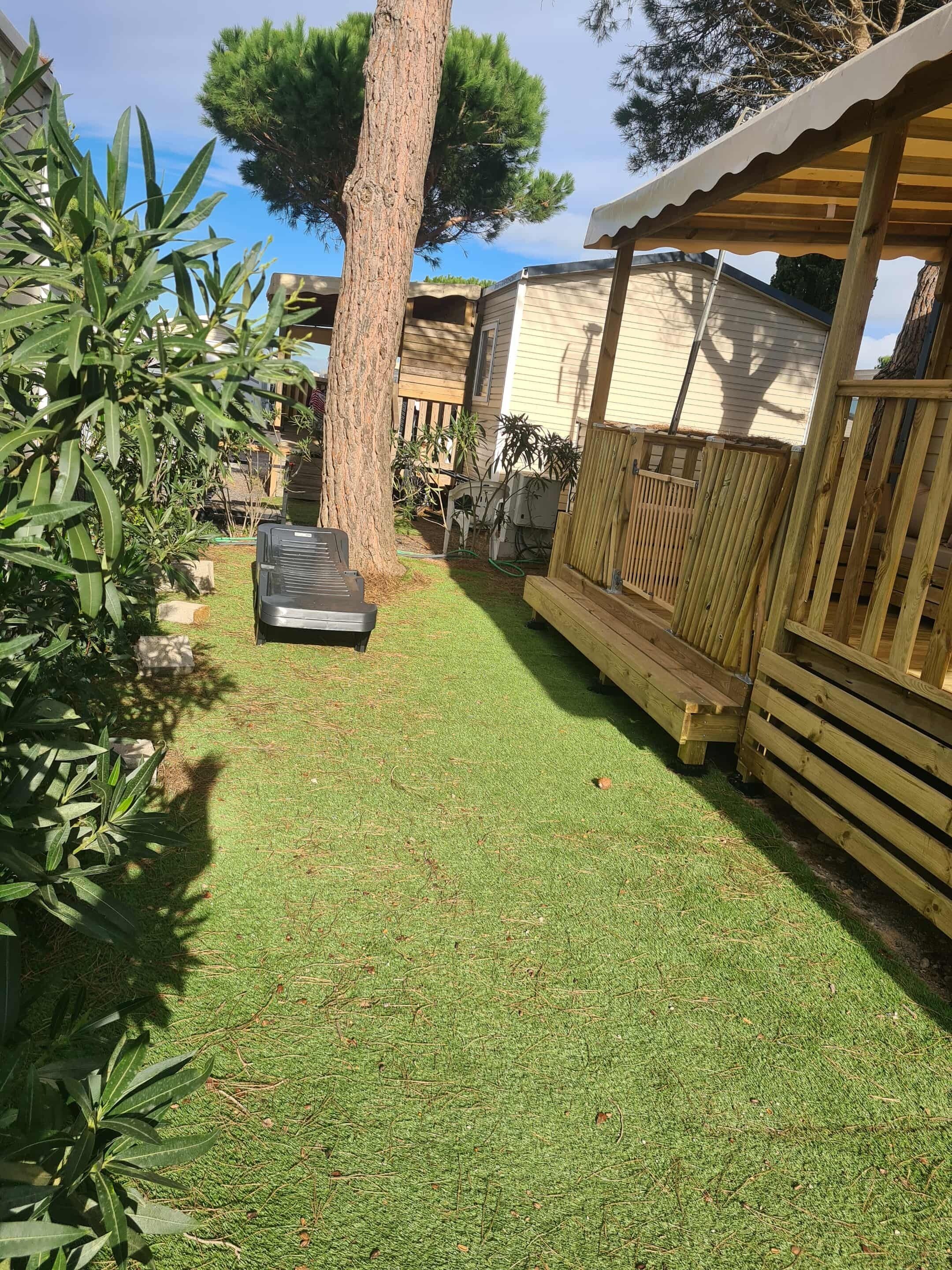 Un patio trasero con una terraza de madera, un árbol y un cobertizo pequeño.