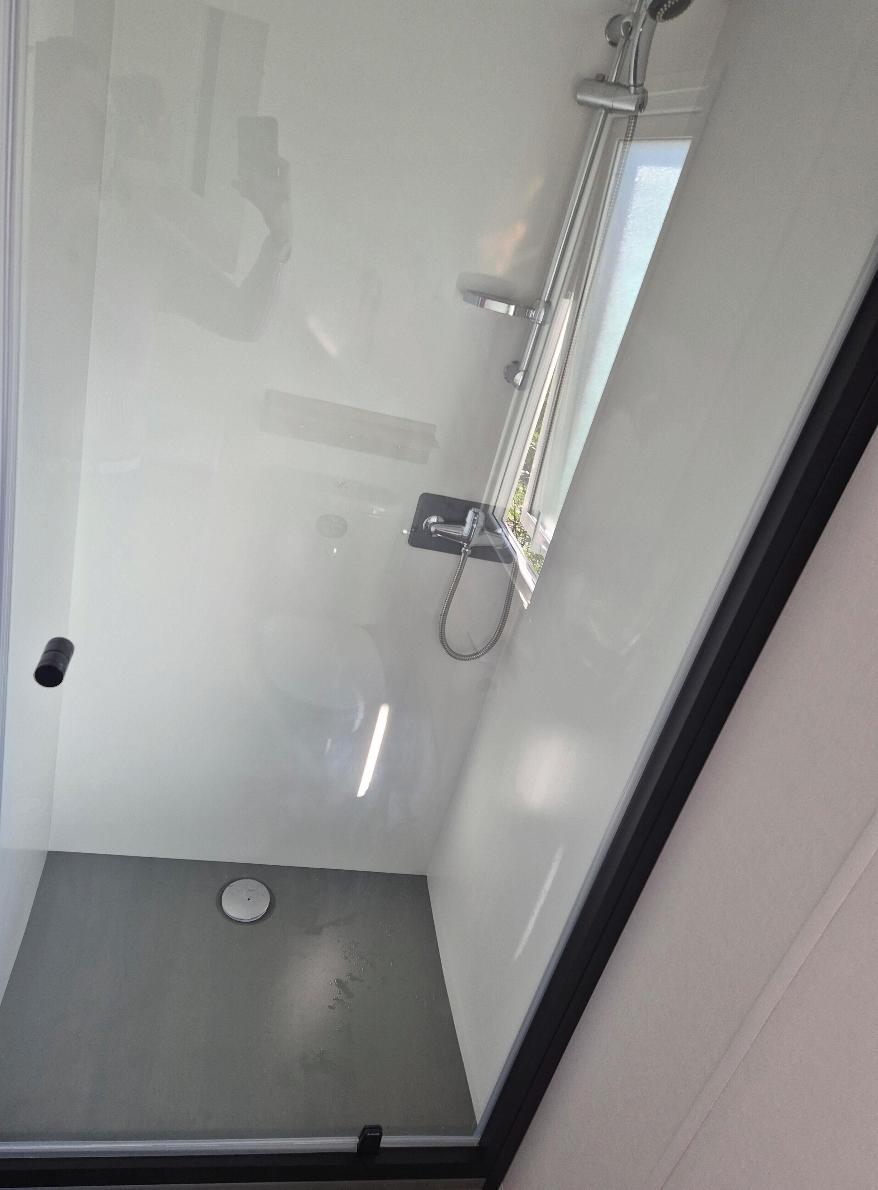 A glass-enclosed shower area with a handheld showerhead and a wall-mounted faucet.