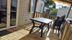 A wooden deck with a table and chairs, a sliding glass door, and a covered area with a wooden railing. - Mobile home near the sea, Camping 4* Mar Estang (Canet-en-Roussillon)