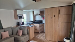 A compact living space with a kitchenette, a sofa, a dining table, and a trash bin. - Mobile home near the sea, Camping 4* Mar Estang (Canet-en-Roussillon)