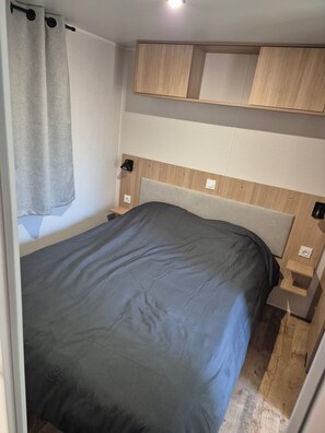 Quarto compacto com cama, cabeceira de madeira, mesas de cabeceira e cortina.