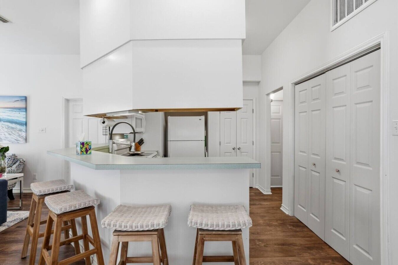 A modern kitchen with a central island, bar stools, and a view of a hallway with white doors.