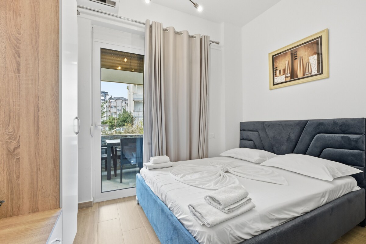 A bedroom with a bed, a view of the outside, a painting on the wall, and a sliding door.