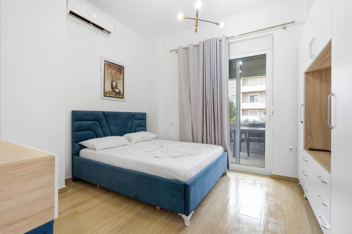 Un dormitorio con cama, escritorio, armario, un cuadro y una puerta corrediza de vidrio al exterior.
