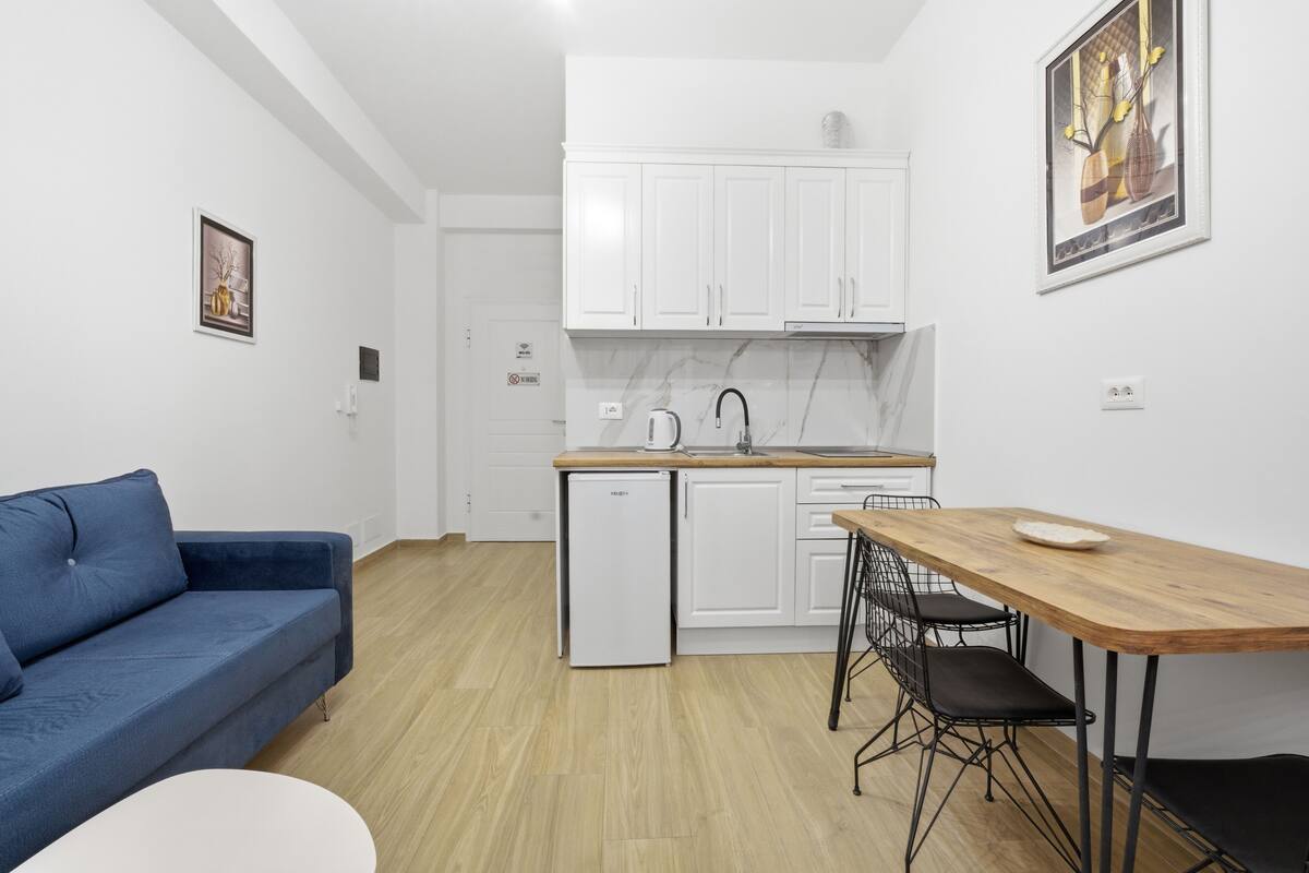 Un espacio habitable pequeño con kitchenette, una mesa de comedor con sillas, un sofá y un refrigerador pequeño.
