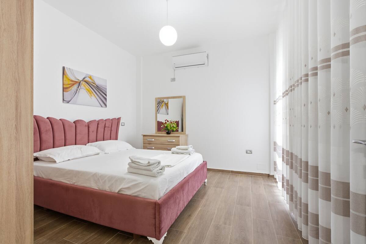 Un dormitorio con cama, mesita de noche, espejo y aire acondicionado de pared.