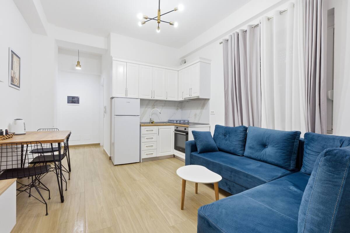 Un espacio habitable compacto con kitchenette, comedor y un sofá azul.
