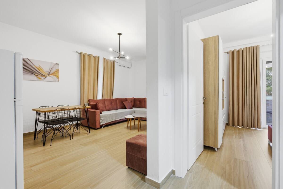 Una sala moderna con un sofá, una mesa de comedor con sillas, una lámpara en el techo y una puerta que da a otra habitación.