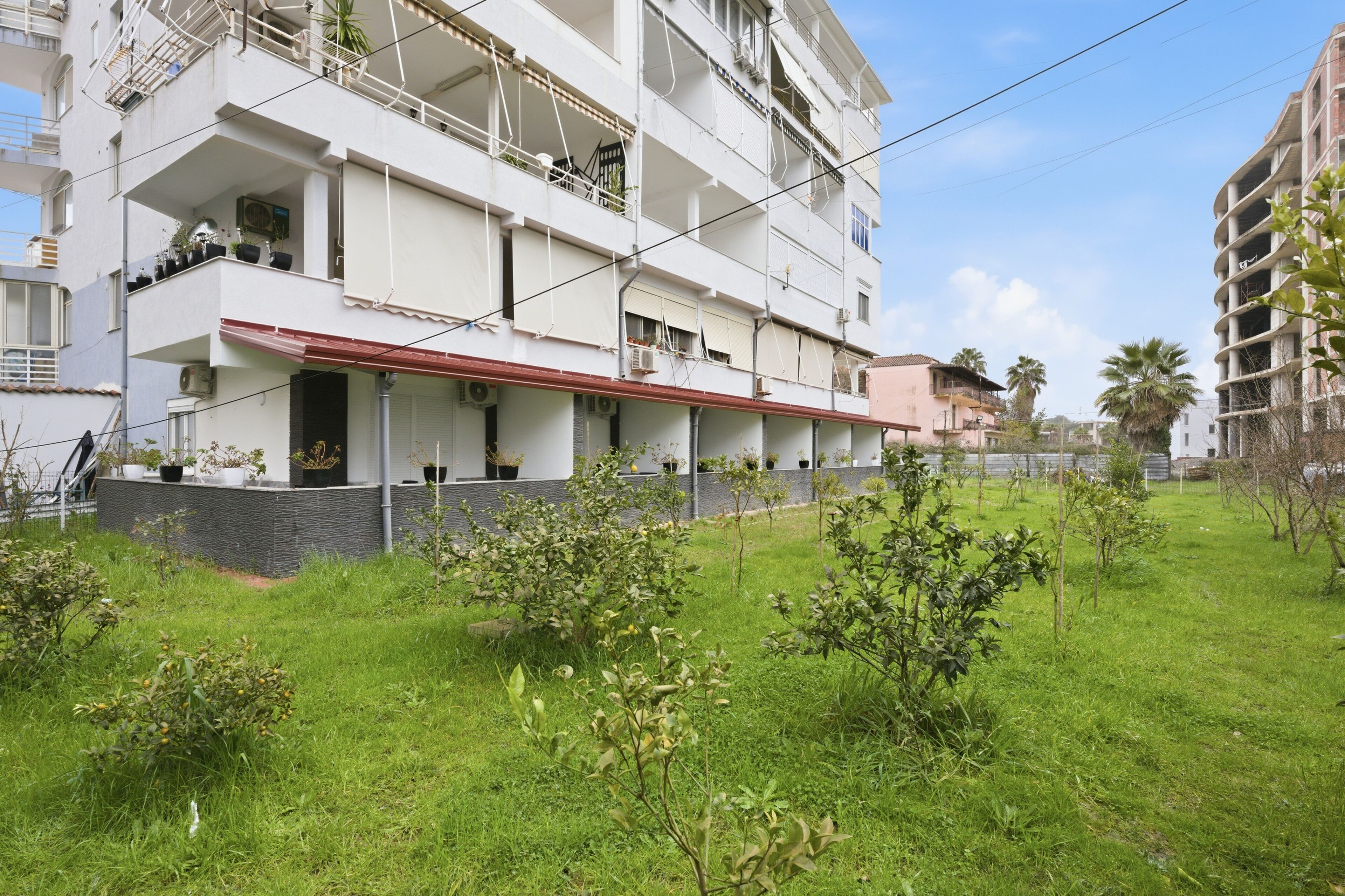 A multi-story residential building with balconies, a red awning, and a grassy courtyard.