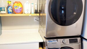 A laundry area with stacked washers and dryers, a shelf with cleaning products, and a white cabinet. - The Cozy Nook- Adorable 2 Bedroom Home (Columbia Falls)