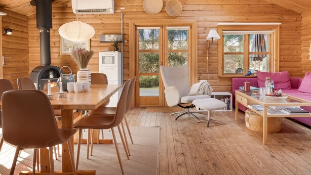 A wooden cabin interior with a dining area, a sofa, a table with books, and a fireplace. - "Tjarko" - 690m to the fjord by Interhome (Storvorde)