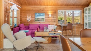 A cozy cabin interior with a wooden ceiling, a sofa, a coffee table, a dining table, and a view through the windows. - "Tjarko" - 690m to the fjord by Interhome (Storvorde)