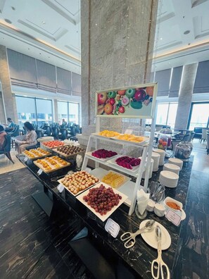 A buffet with various food items, a fruit display, and a large pillar in the center. - Luxury Apartment Seaside (Da Nang)