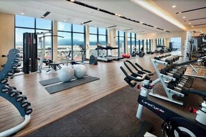 A gym with cardio machines, weights, and exercise balls, with large windows offering a city view. - Luxury Apartment Seaside (Da Nang)