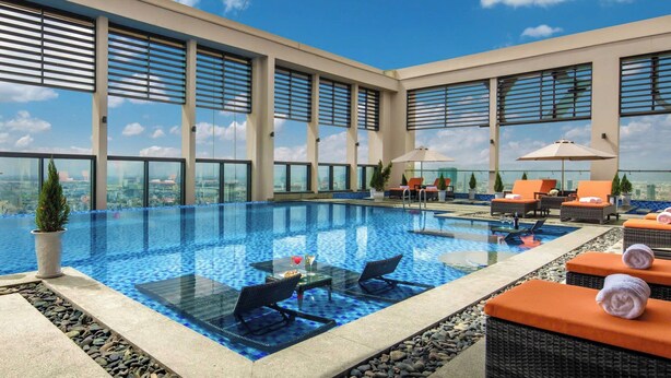 Ein Rooftop-Pool mit Infinity-Kante, Liegestühlen und Sonnenschirmen, großen Fenstern und freiem Blick auf die Stadtlandschaft.