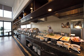 A buffet setup with a chef preparing food, a variety of dishes, and a modern kitchen area. - Luxury Apartment Seaside (Da Nang)