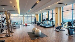 Ein Fitnessstudio mit Cardiogeräten, Gewichtstrainern und großen Fenstern mit Blick auf die Stadt.