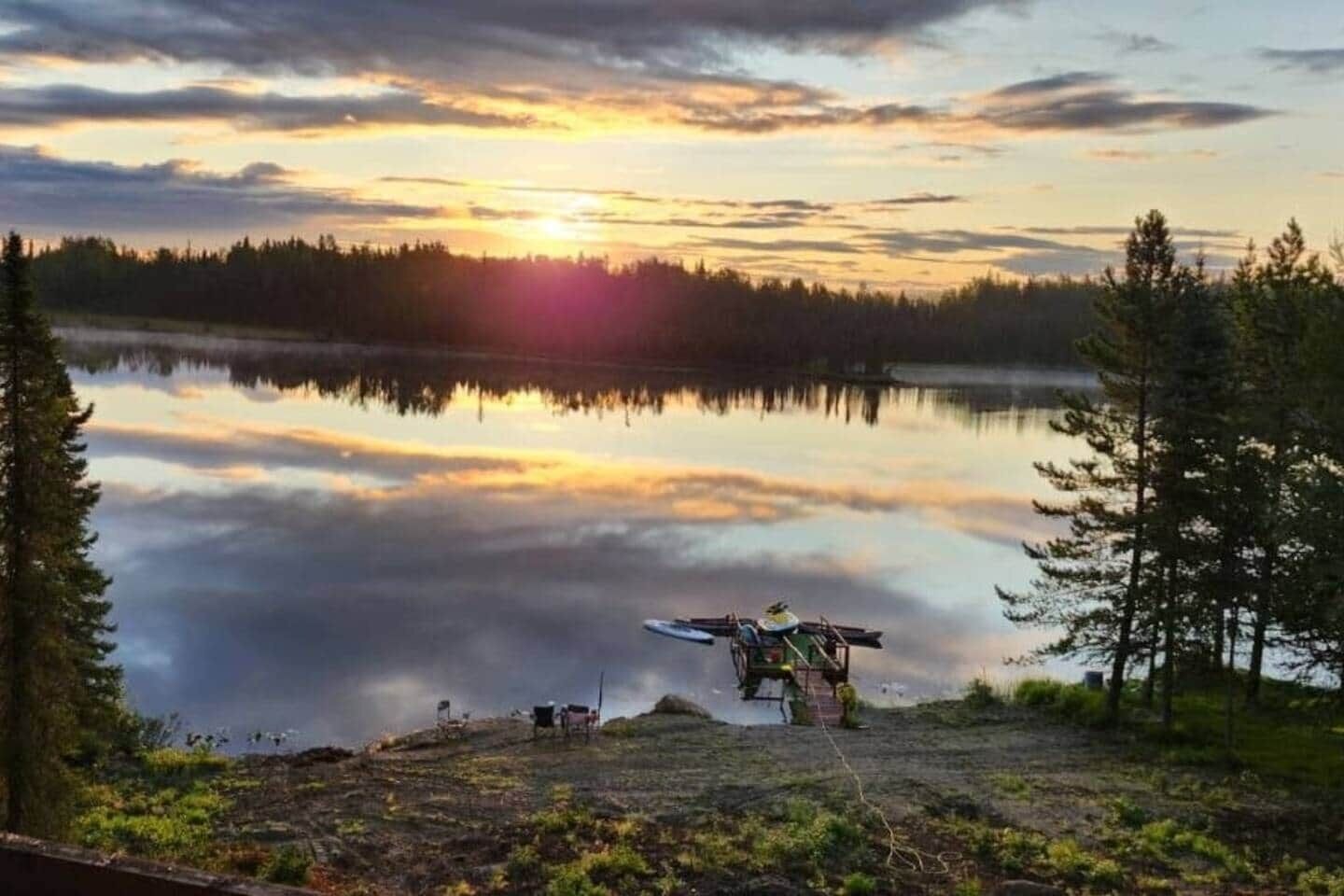 Un lac paisible au coucher du soleil, avec un canoë et du matériel sur la rive.