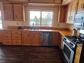 Una cocina con gabinetes de madera, lavavajillas de acero inoxidable, estufa y ventana con vistas a árboles.