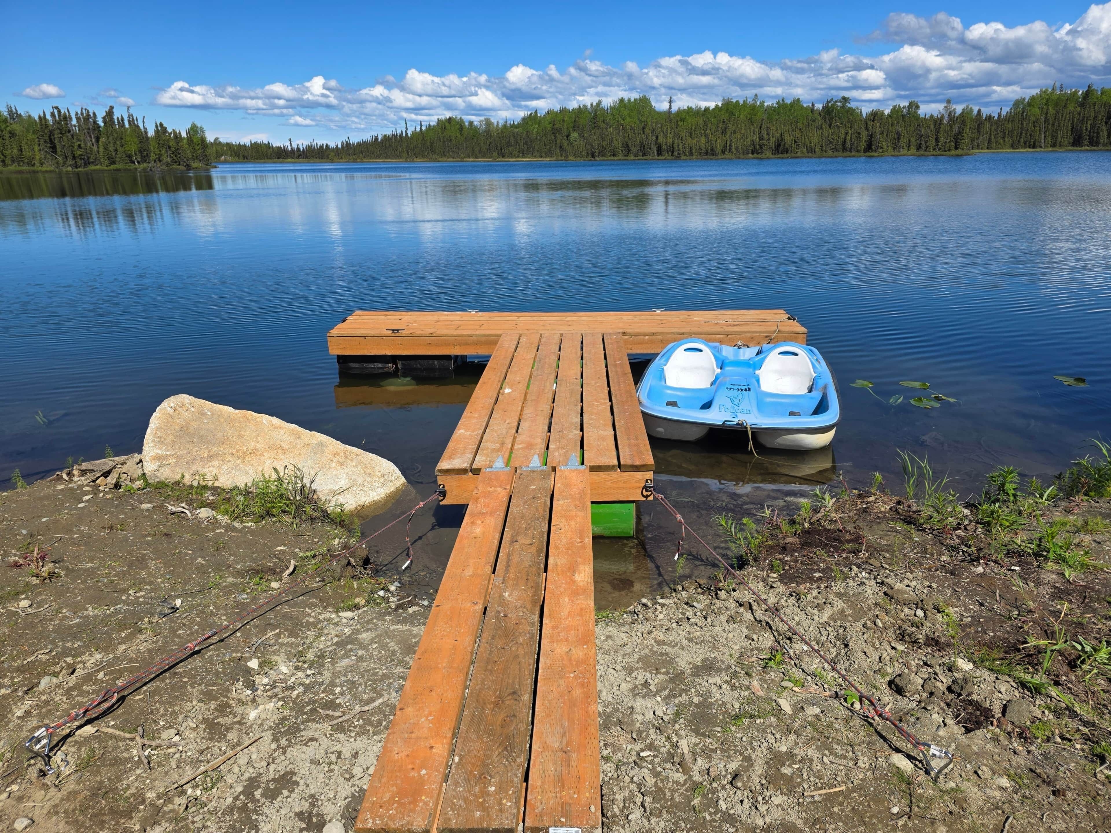 A wooden dock with a boat and a large rock.