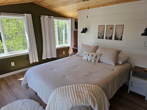 Um quarto com uma cama grande, uma mesa de cabeceira, uma luminária e uma janela com cortinas.