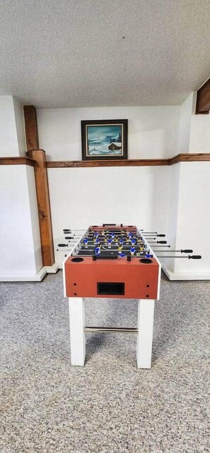 A foosball table in a room with a carpeted floor, white walls, and a framed picture on the wall. - Spacious house near Soldotna, AK (Ridgeway)