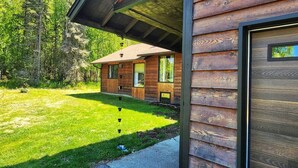 Una cabaña de madera con un porche cubierto, un patio con césped y un paisaje de bosque al fondo.