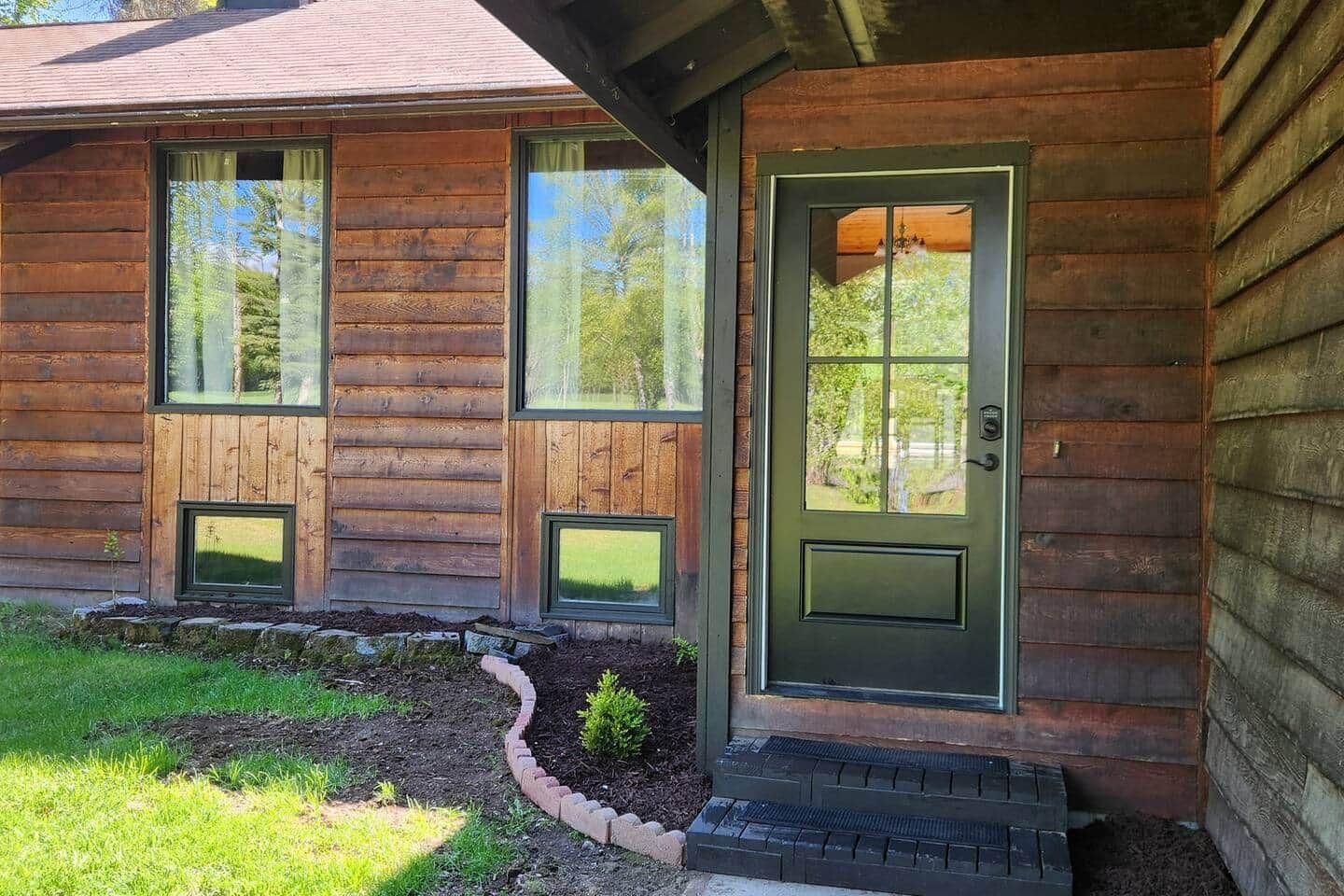 A wooden cabin with a green door, two windows, and a small porch area.