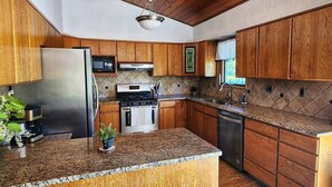 Una cocina con armarios de madera, encimera de granito, electrodomésticos de acero inoxidable y una lámpara colgante.