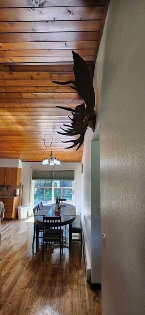 A dining area with a wooden ceiling, a chandelier, and a large window. - Spacious house near Soldotna, AK (Ridgeway)