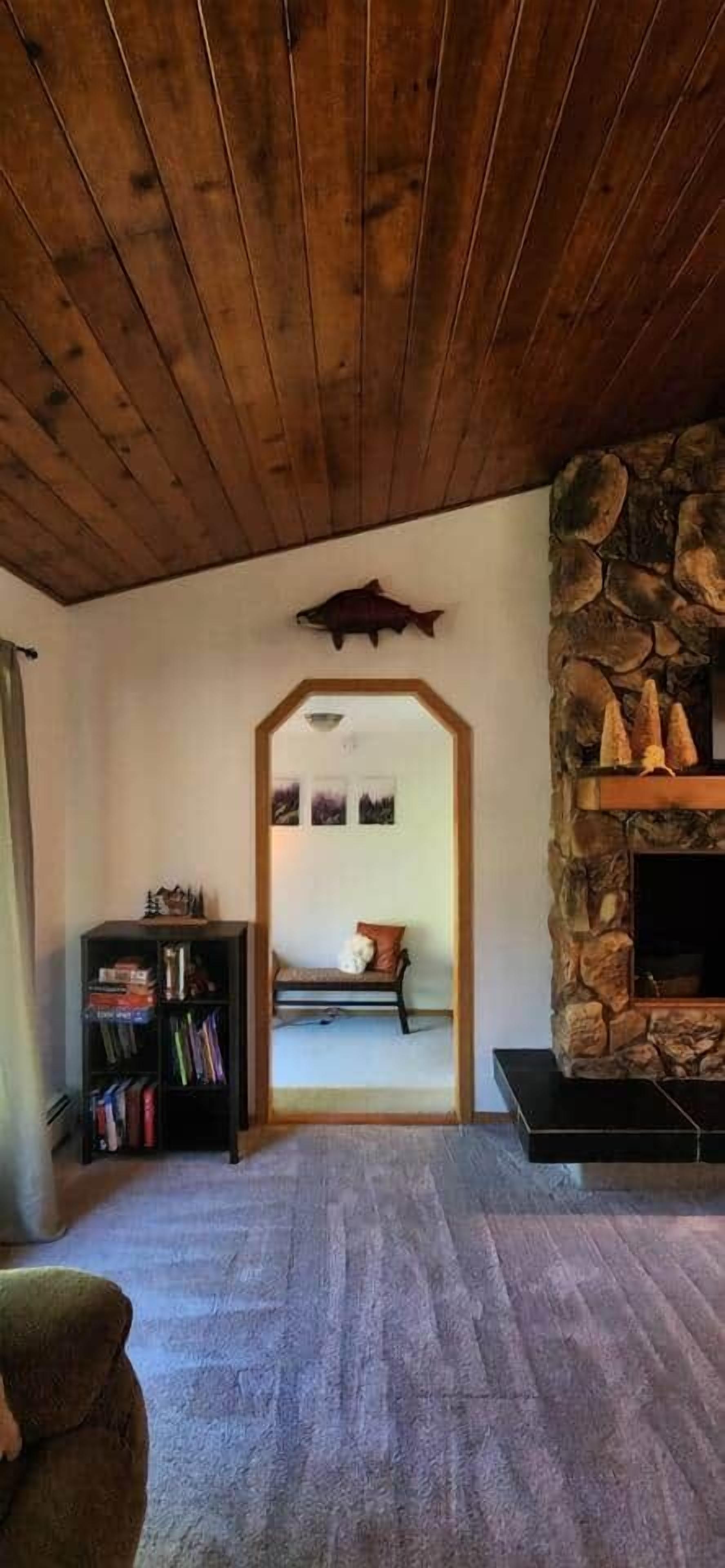 A living room with a stone fireplace, wooden ceiling, and a bookshelf.