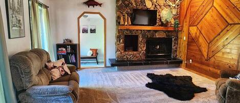 A cozy living room with a stone fireplace, a couch, a rug, and a television.