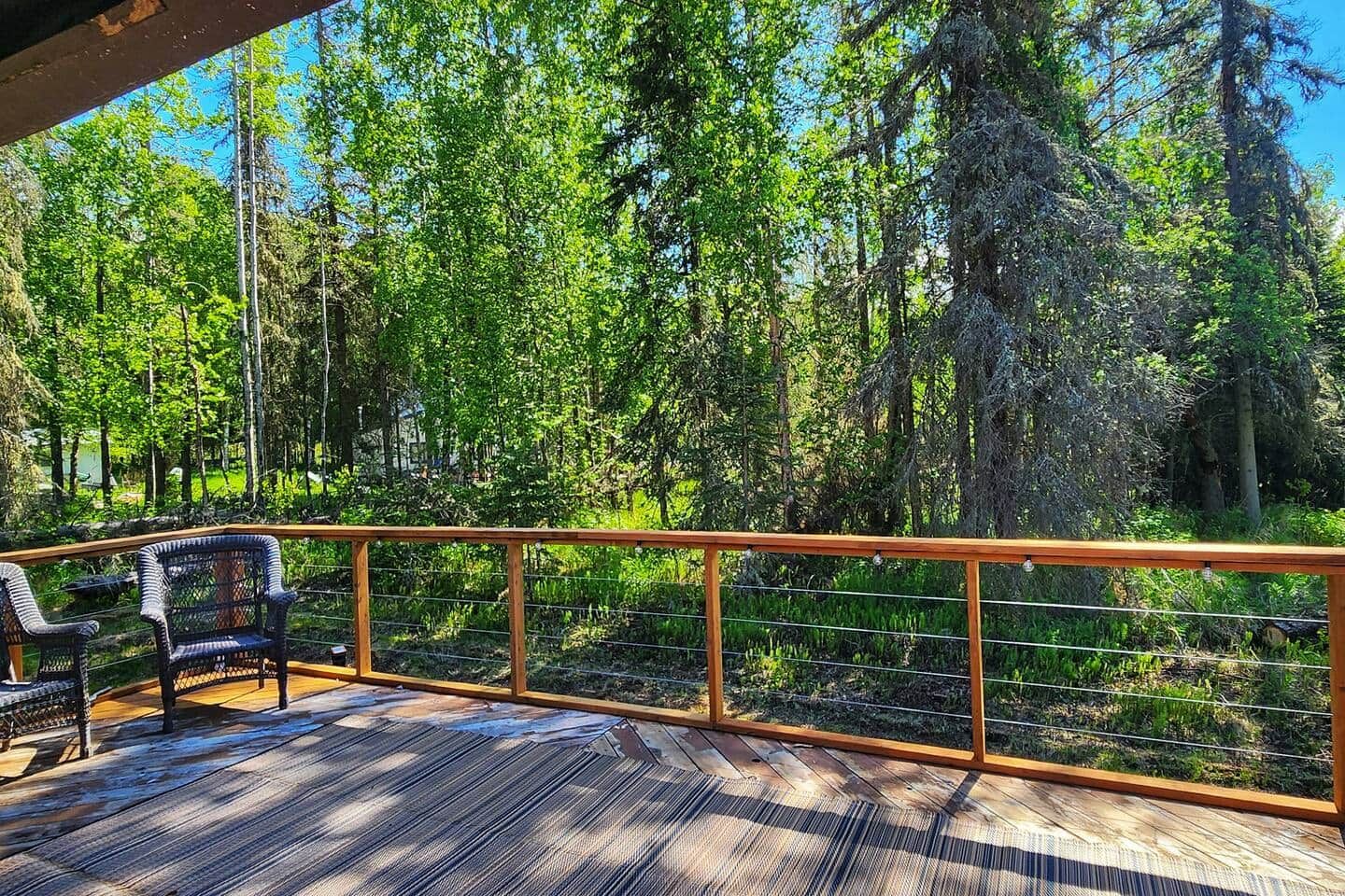 A wooden deck with a railing, surrounded by dense forest.