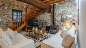 A cozy living room with a stone wall, wooden staircase, fireplace, and a sofa. - Domaine Le Pehau 4 - Avec jardin et terrasse (Osserain-Rivareyte)