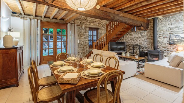 A rustic interior with a wooden dining table set for four, a stone fireplace, and a cozy living area with a sofa and TV. - Domaine Le Pehau 4 - Avec jardin et terrasse (Osserain-Rivareyte)