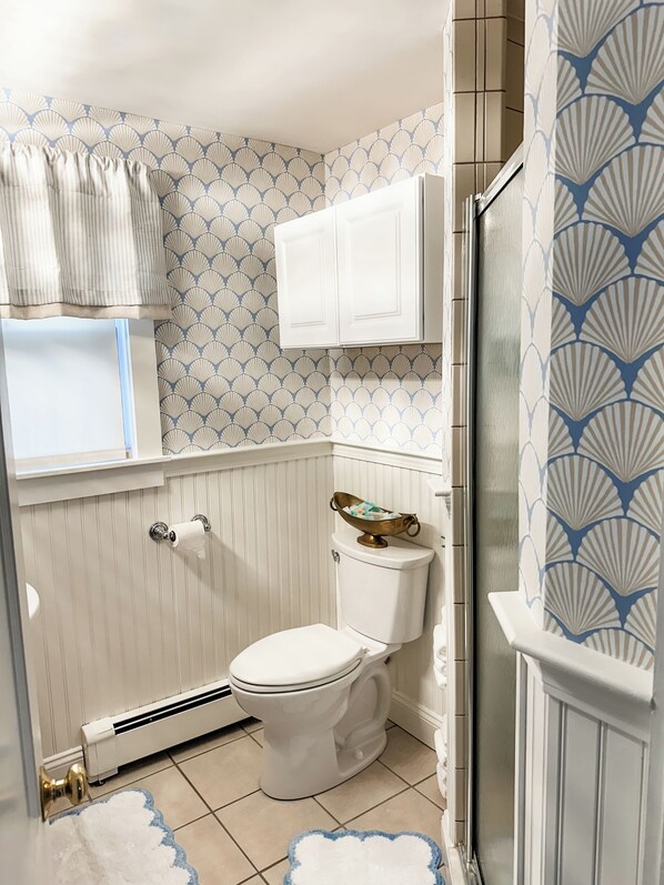 Un baño con inodoro, radiador, ventana con cortina y pared decorada.