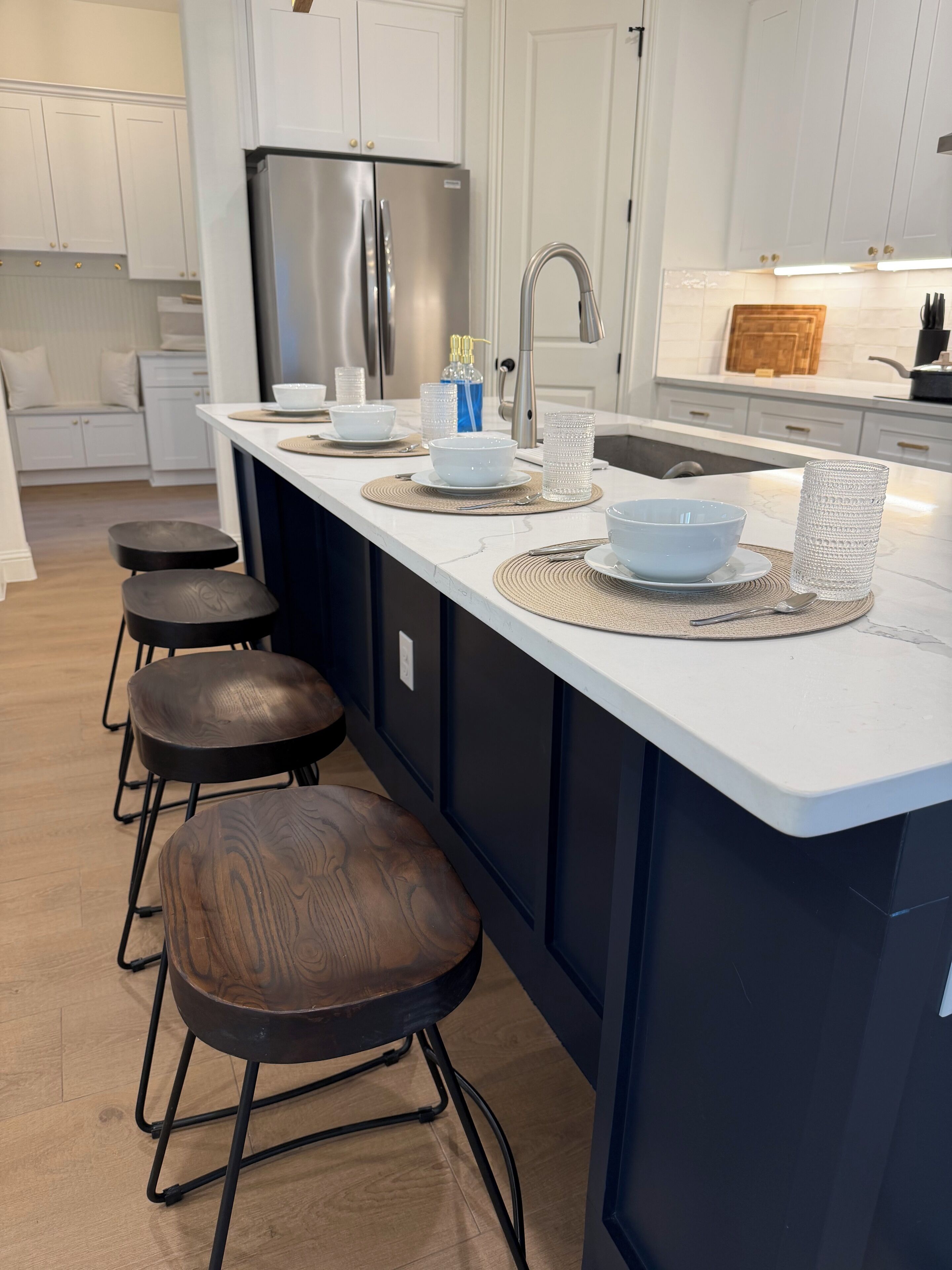 Una cocina moderna con una isla central, taburetes de bar, un refrigerador de acero inoxidable y un lavamanos.