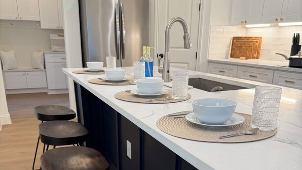 Moderni keittiö, jossa on keskeinen keittiösaareke, baarituolit, ruostumattomasta teräksestä valmistettu jääkaappi ja pesuallas.