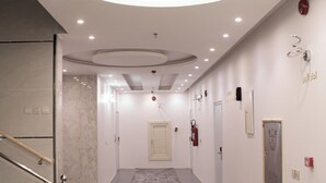 A modern hotel hallway with a marble floor, a glass railing, a circular ceiling light, and a door at the end.