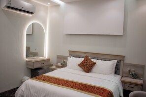 A hotel room with a bed, a bedside table, a nightstand, a mirror, and an air conditioning unit.