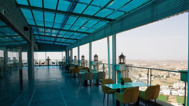 A rooftop terrace with tables and chairs, large windows, and a view of the city.