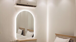 A hotel room with a bed, a bedside table, a mirror, and an air conditioning unit.