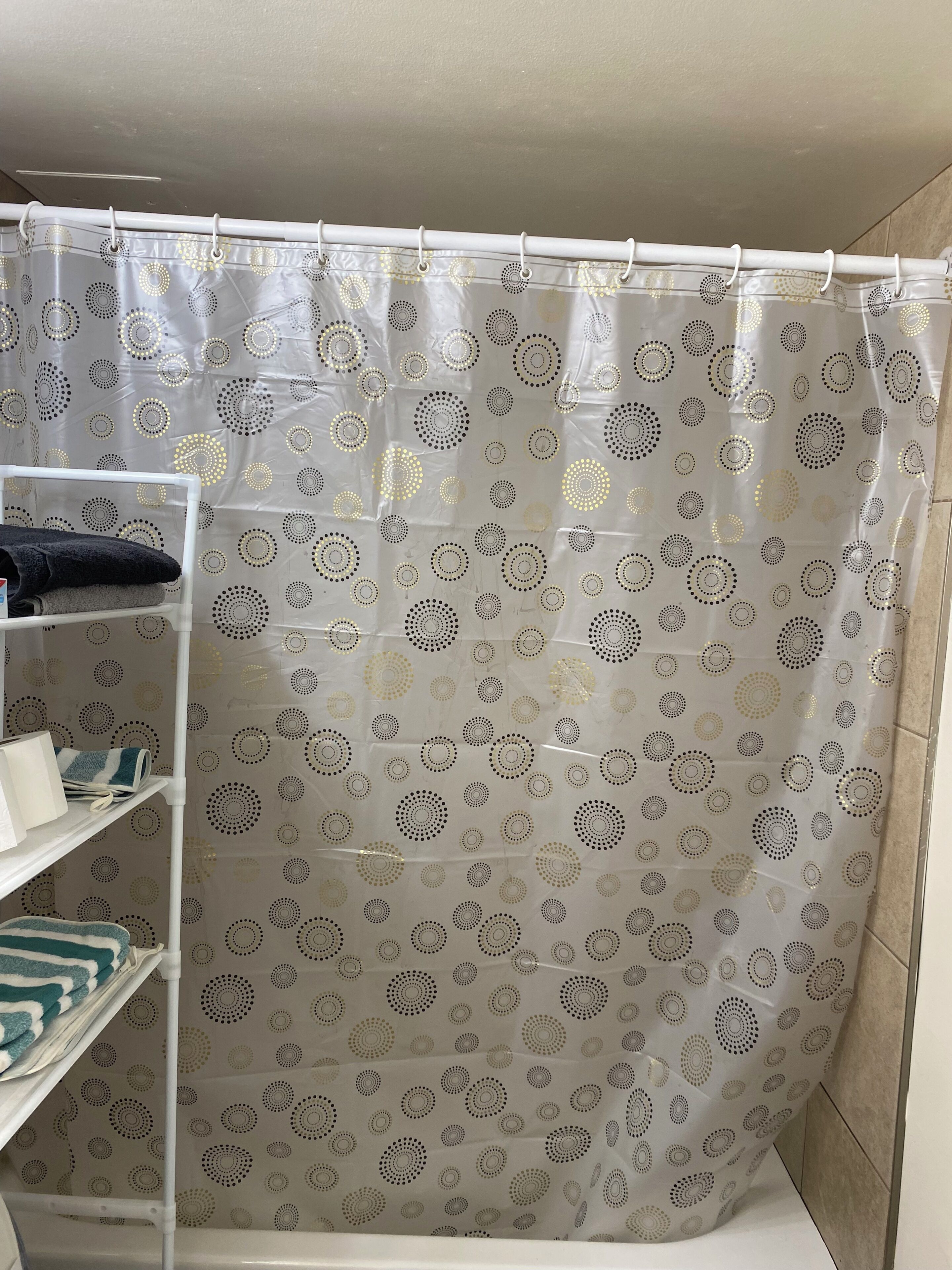 Un rideau de douche orné d’un motif circulaire, un porte-serviettes blanc et une étagère avec des serviettes pliées.