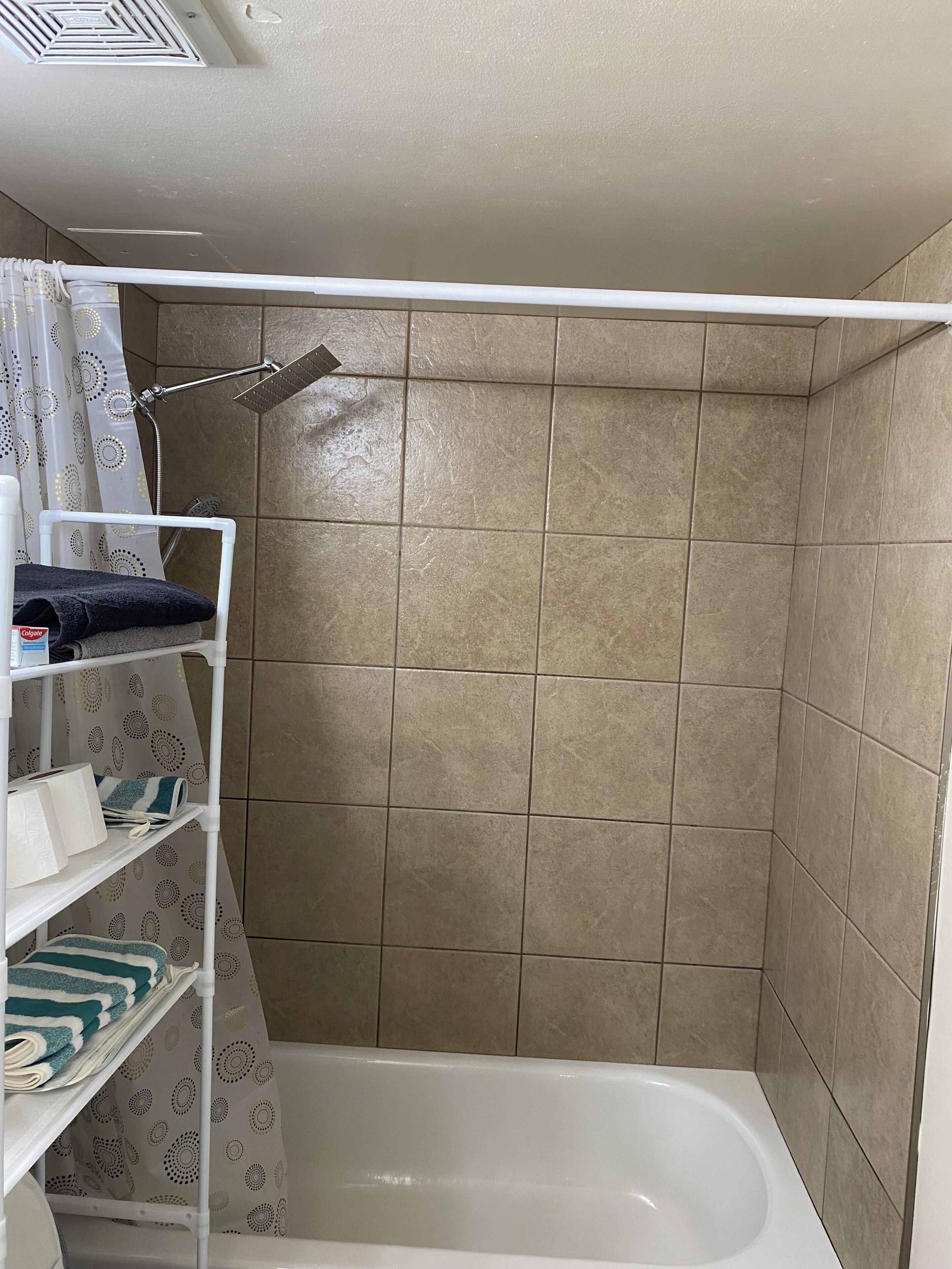 Un baño con ducha, paredes con azulejos, una bañera blanca y repisas con toallas y artículos de aseo.