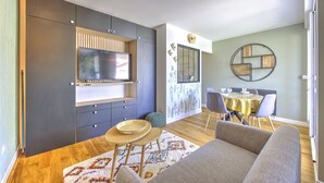 A modern living room with a flat-screen TV, a dining area with a yellow tablecloth, and a patterned rug. - Brousse & Brise - Studio à deux pas de la mer (Arcachon)