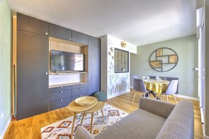 A modern living room with a flat-screen TV, a dining area with a yellow tablecloth, and a patterned rug. - Brousse & Brise - Studio à deux pas de la mer (Arcachon)