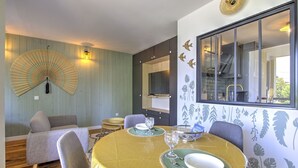 A dining area with a round table, chairs, a fan, and a view of a staircase. - Brousse & Brise - Studio à deux pas de la mer (Arcachon)