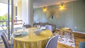 A dining area with a round table, chairs, a fan, and a view through a glass door. - Brousse & Brise - Studio à deux pas de la mer (Arcachon)
